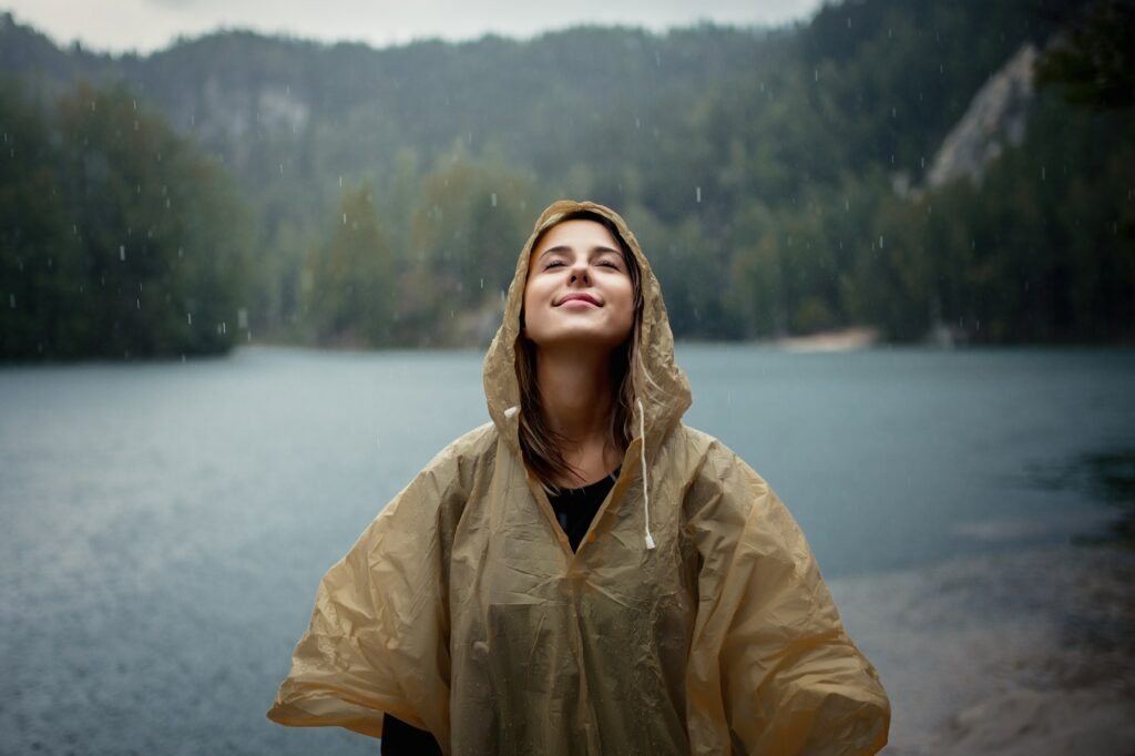 woman in raincoat near lake in rainy day.